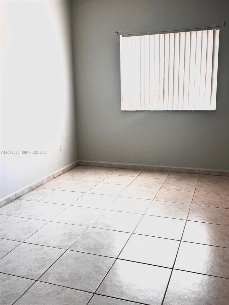 Neutral-toned interior space featuring light-colored square floor tile and a window with vertical blinds