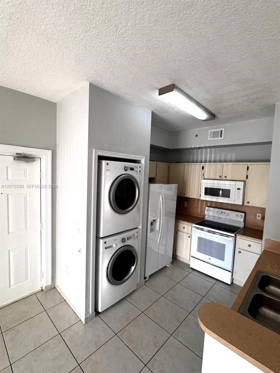 Kitchen featuring white cabinetry, solid-surface countertops, built-in microwave, range, and stacked laundry unit