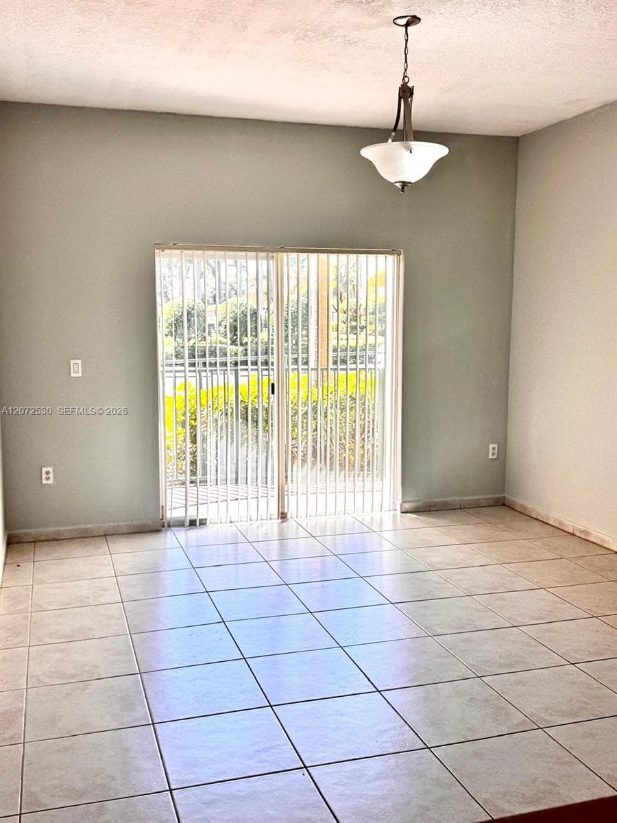 Interior room featuring tile flooring, neutral wall paint, a metal and glass pendant light fixture, and sliding glass doors with vertical blinds