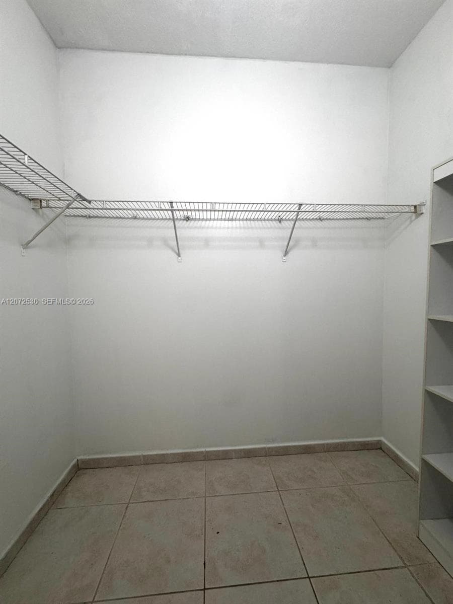 Walk-in closet featuring floor-to-ceiling tile flooring, built-in shelving unit, and wire rack storage