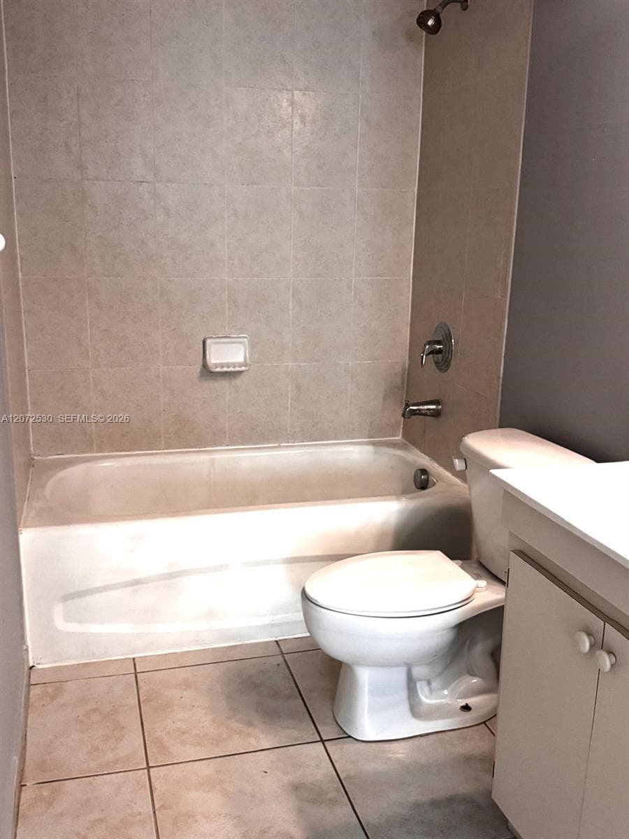 Bathroom featuring a standard soaking tub, shower head with wall-mounted controls, built-in soap niche, tile flooring, and a vanity cabinet