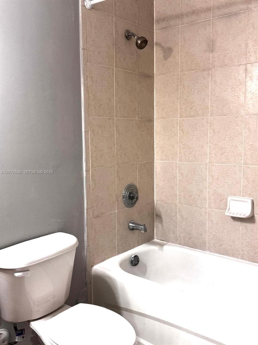 Full bathtub enclosure featuring neutral ceramic wall tiling, integrated soap dish, and chrome-finish hardware