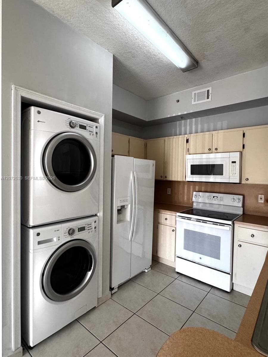Kitchen featuring tile flooring, neutral cabinetry, white built-in appliances, and a stacked laundry unit