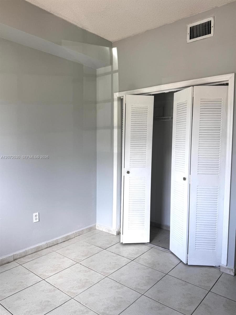 Room featuring neutral walls, light-toned ceramic tile flooring, and a closet with white louvered bi-fold doors