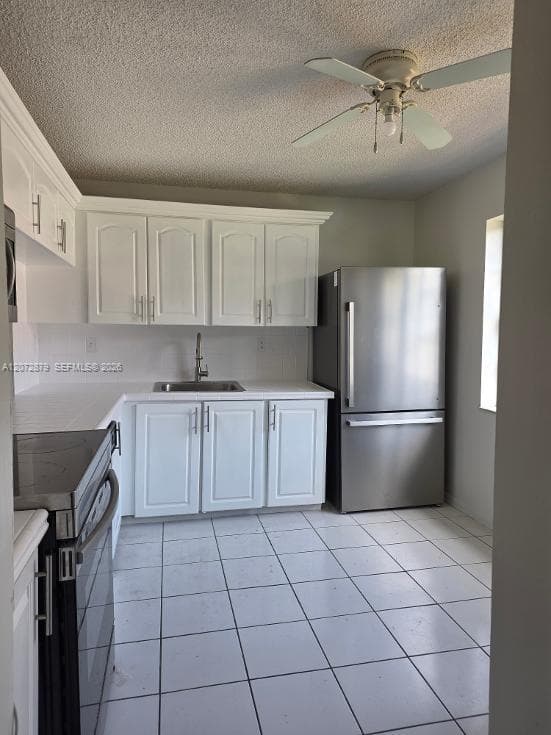 Kitchen featuring white cabinetry, stainless steel appliances, a corner sink, white tile flooring, and a ceiling fan