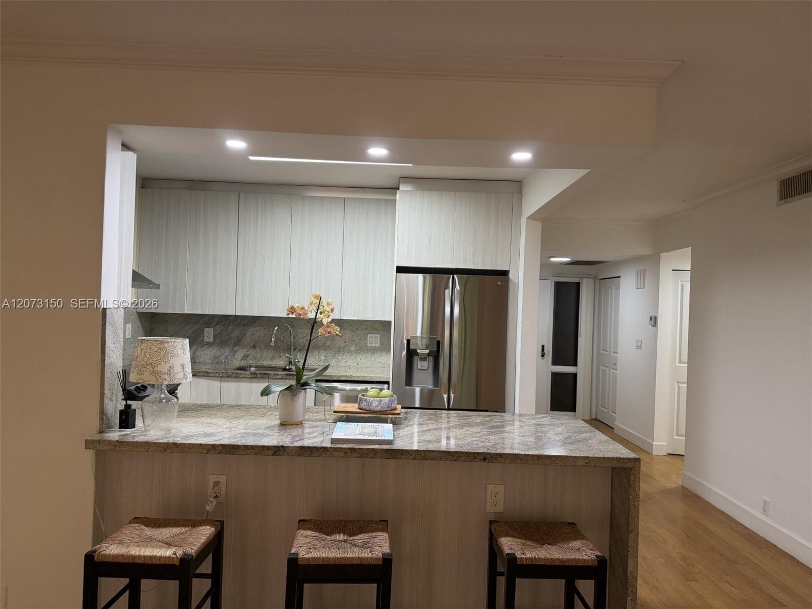 Kitchen featuring light-toned cabinetry, stone-finish countertops with a waterfall edge, stainless steel appliances, a stainless steel range hood, and wood-finish flooring