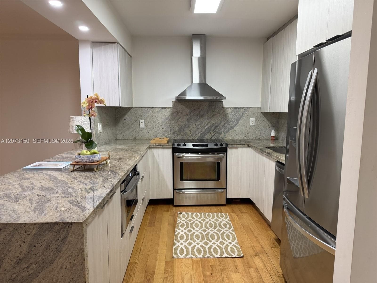 Kitchen featuring light-toned cabinetry, stainless steel appliances, stone countertops, stone backsplash, and wood-finish flooring