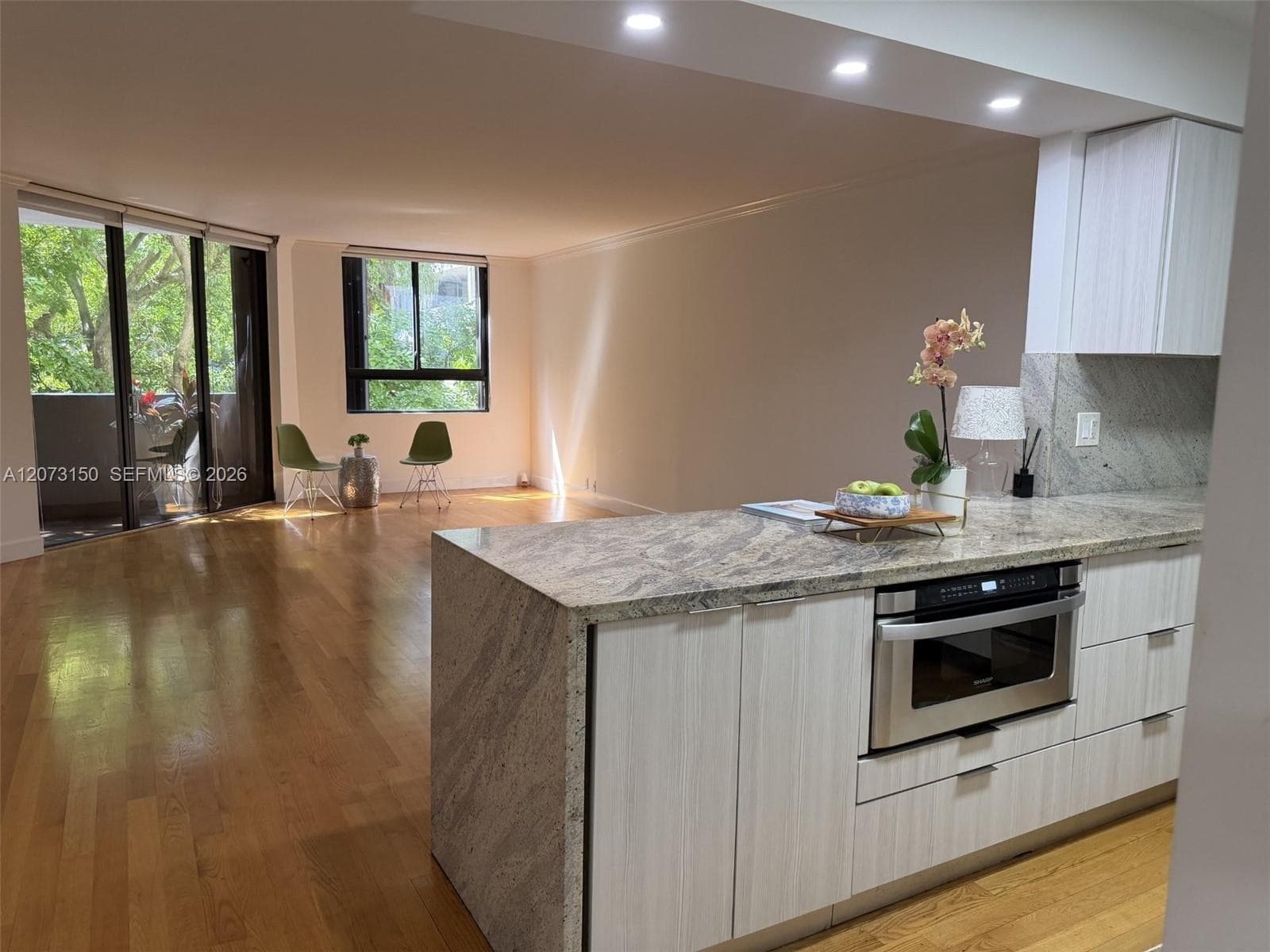 Kitchen featuring a waterfall-edge stone island, light-toned flat-panel cabinetry, stone backsplash, stainless steel range hood, and wood-finish flooring