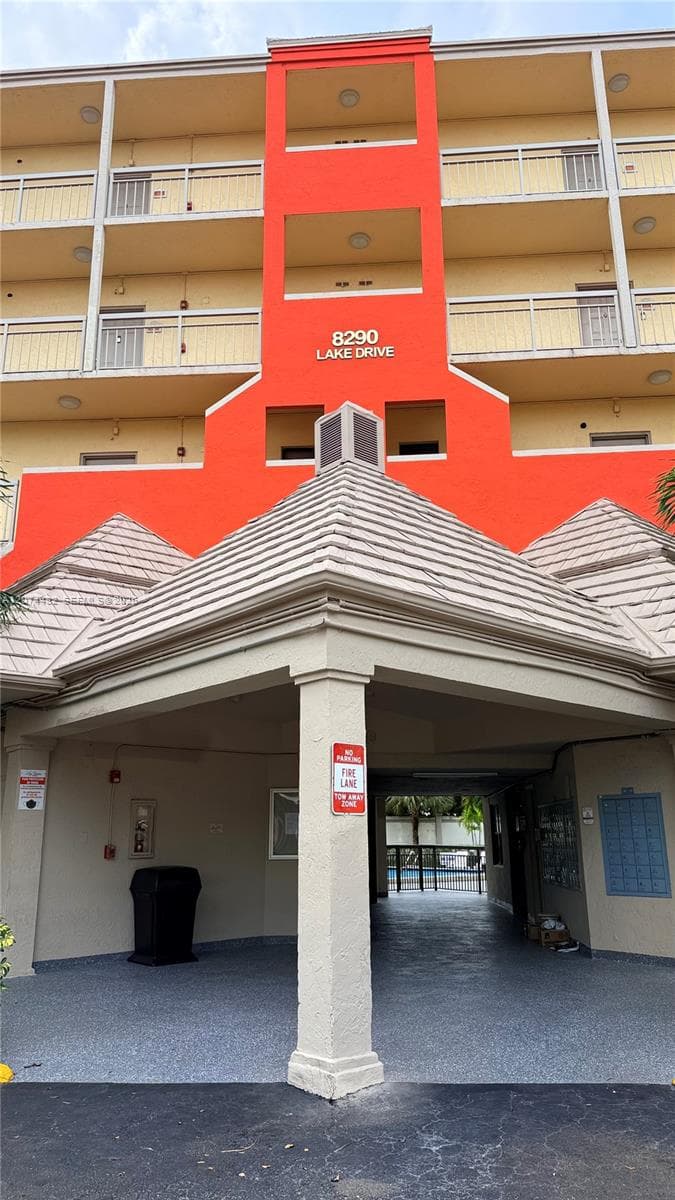 Multi-story exterior featuring a covered entryway with a stone-finish pillar, textured facade, tiered shingled roof lines, and balconies with metal railings