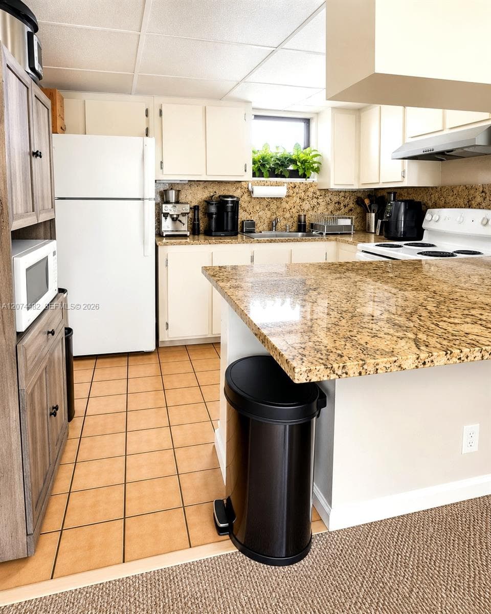 Kitchen featuring stone-patterned countertops, a peninsula with bar seating, tiled flooring, and light-toned cabinetry