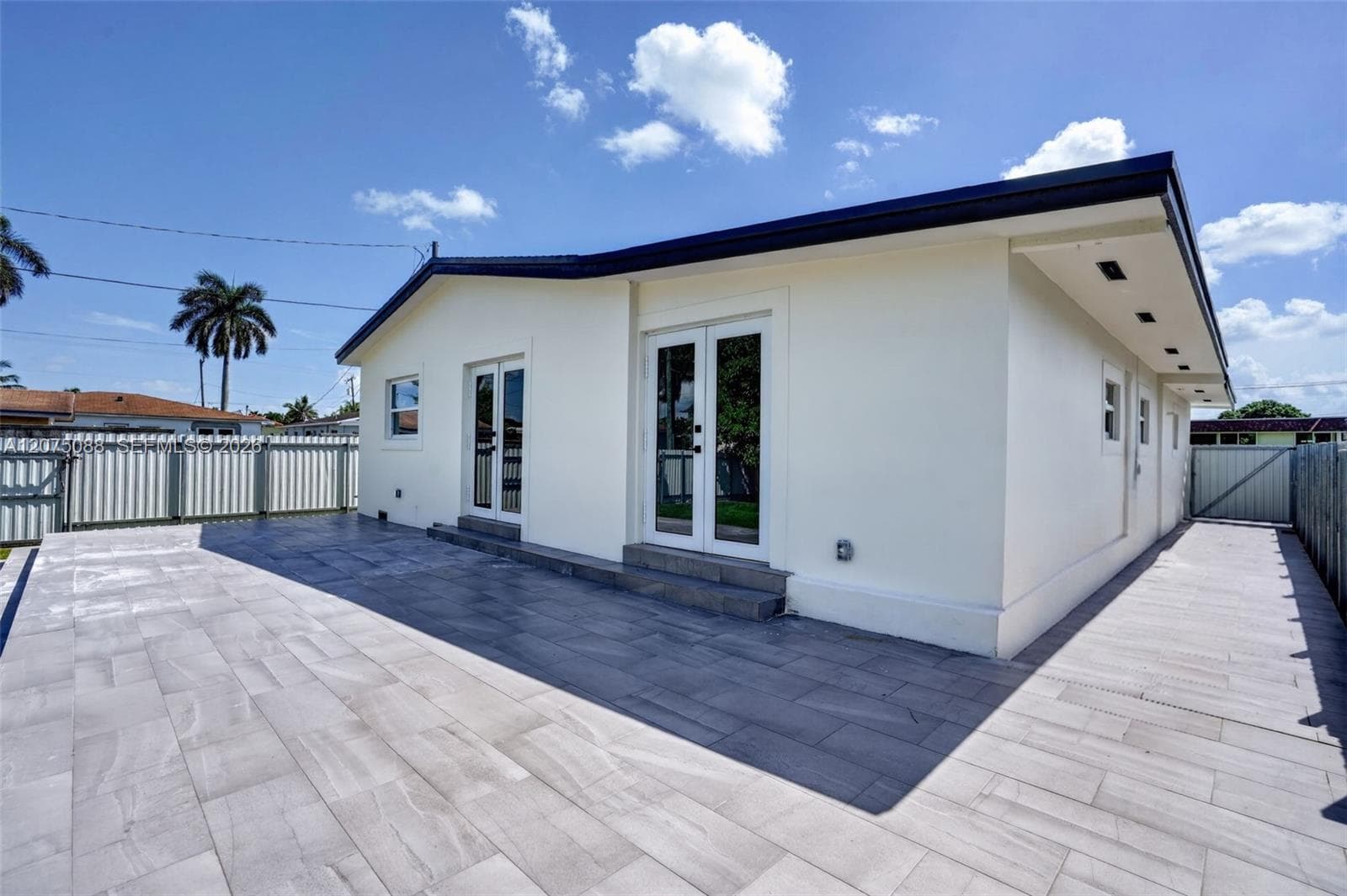 Exterior rear elevation featuring large-format stone-style patio pavers, two sets of white French doors, and perimeter metal privacy fencing
