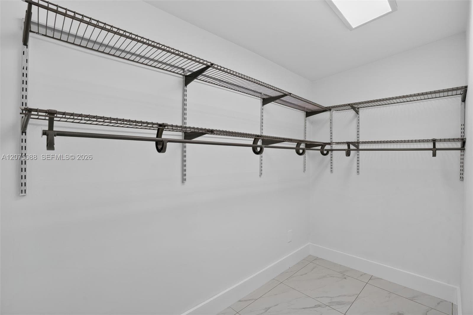 Walk-in closet featuring multi-tiered wire shelving, integrated garment rods, recessed ceiling lighting, and large-format tile flooring
