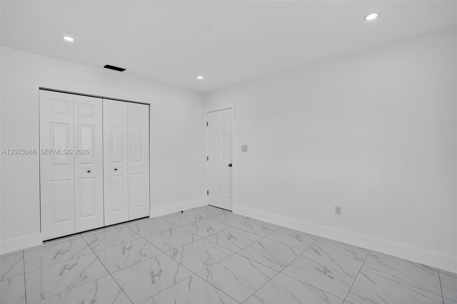 Neutral-toned interior featuring large-format tile flooring with a veined pattern, recessed ceiling lighting, and a double-panel closet with bifold doors