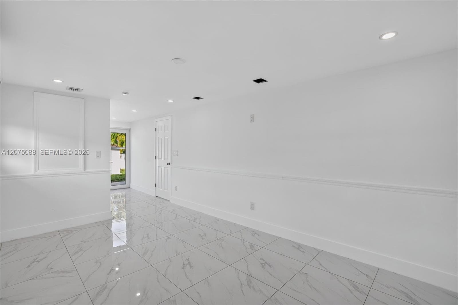 Large-format tile flooring with a neutral-toned veining pattern, crisp white walls, recessed ceiling lighting, and crisp white chair rail molding