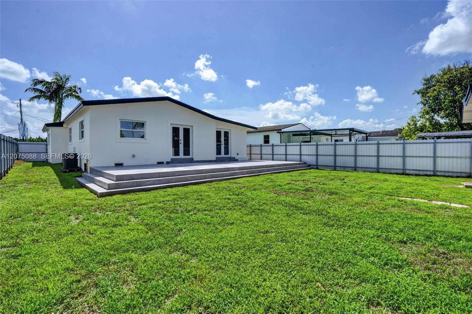 Rear exterior featuring a tiered concrete patio, dual sets of French doors, and full perimeter privacy fencing