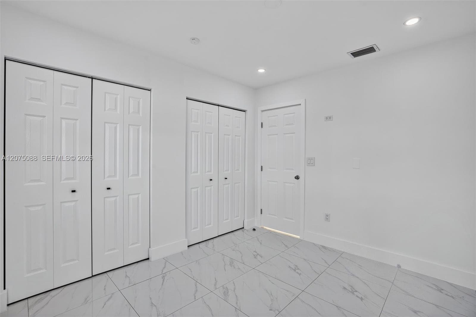 Room featuring large-format tile flooring, dual sets of bi-fold closet doors, a classic interior door, and recessed lighting