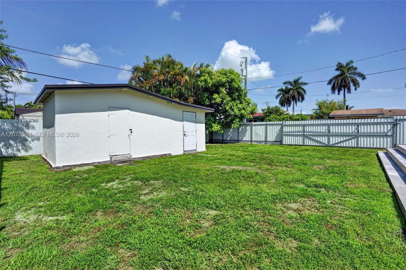 Backyard featuring a detached storage structure, manicured lawn, and perimeter metal fencing