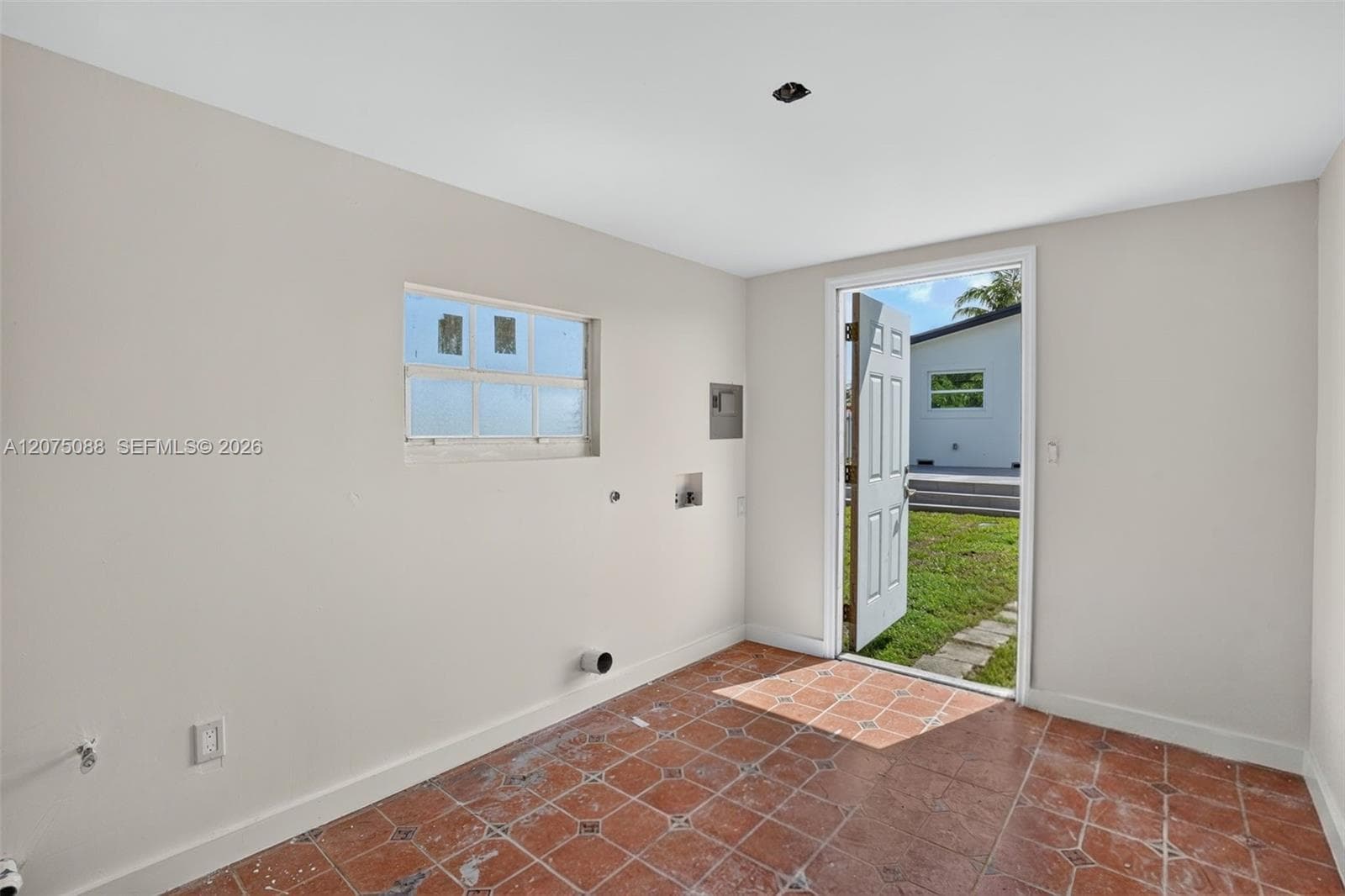 Utility space featuring neutral wall paint, tile flooring with geometric detail, a multi-pane window, and an exterior door
