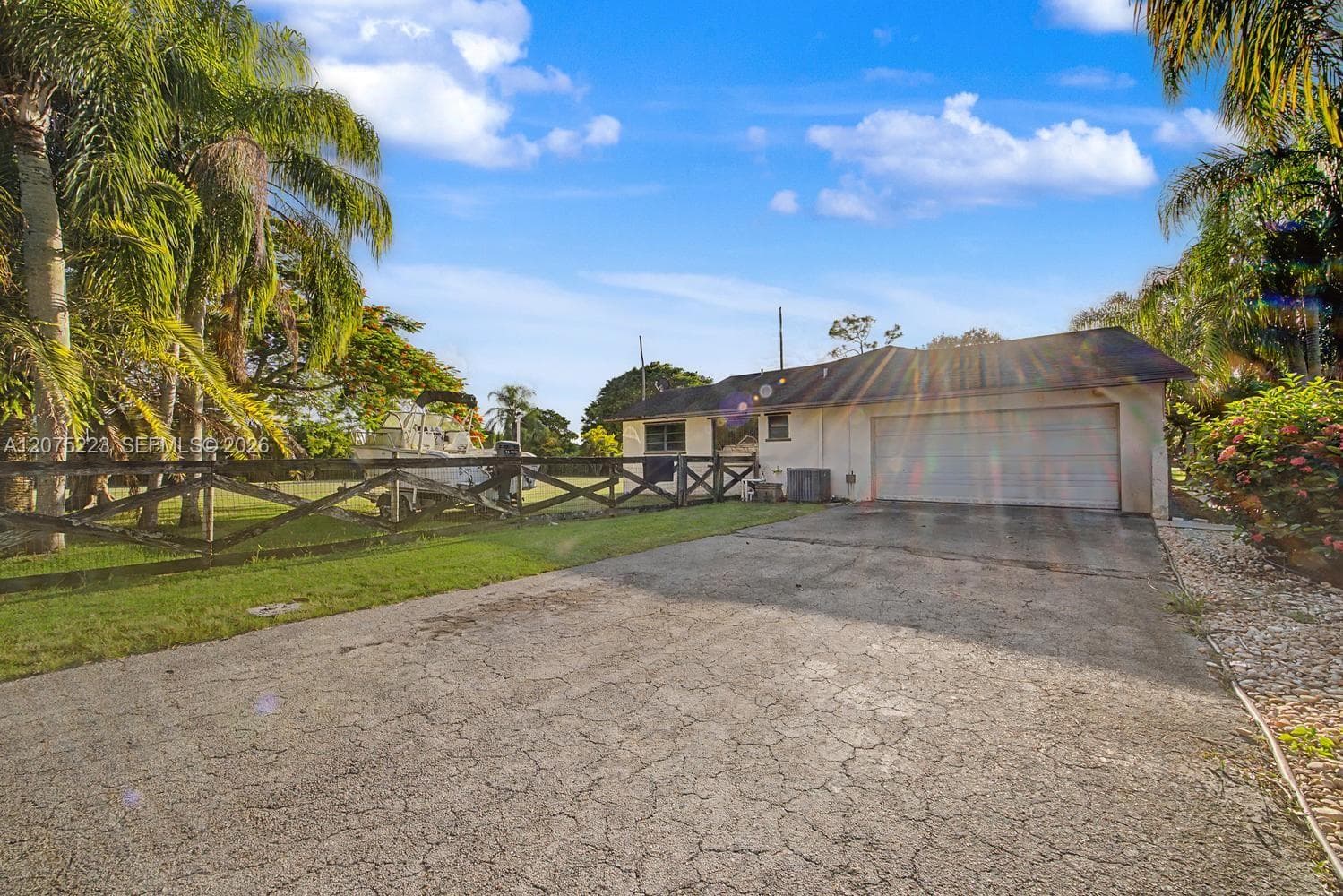 Attached two-car garage with a spacious driveway providing ample parking, surrounded by mature tropical landscaping.