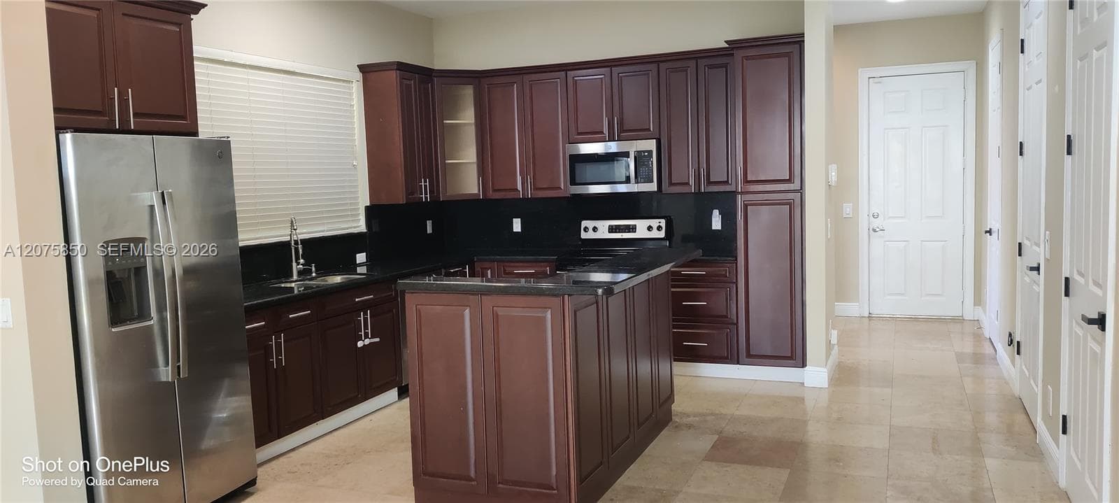 Kitchen featuring dark-toned cabinetry, a center island, stone-finish countertops, stainless steel appliances, and large-format tile flooring