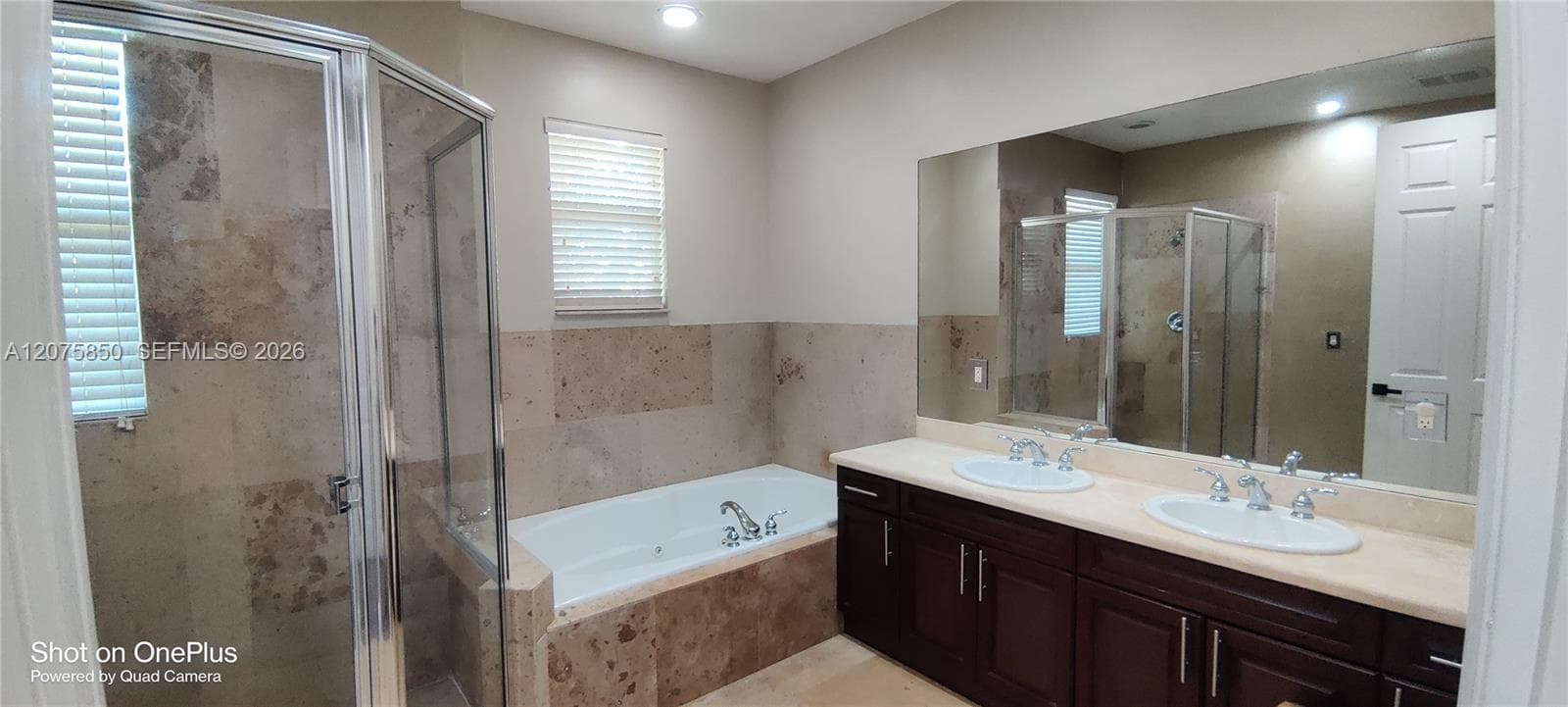 Double vanity with light-toned countertop, dual drop-in sinks, deep soaking tub with tile surround, and separate glass-enclosed shower