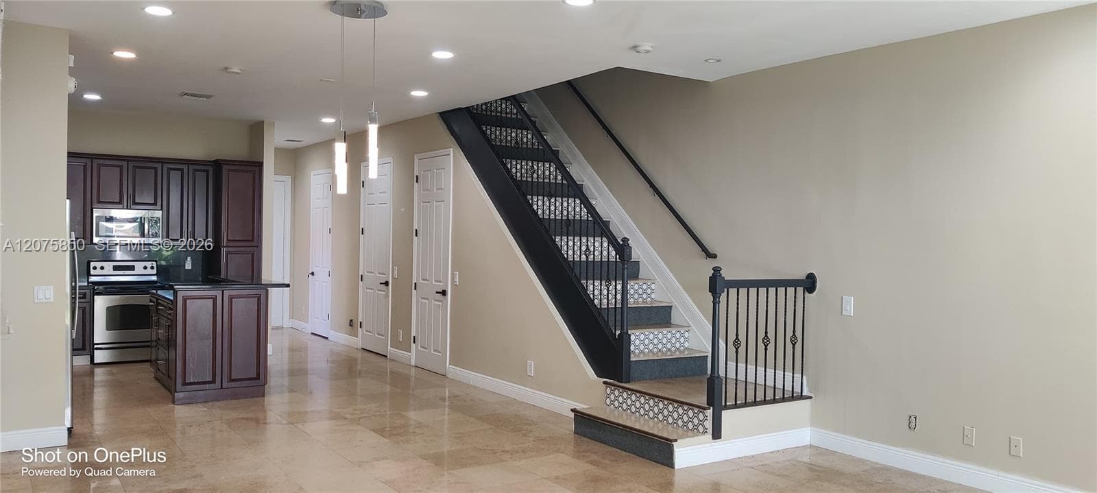 Interior featuring stone-finish tile flooring, custom dark-toned cabinetry, stainless steel kitchen appliances, recessed lighting, and a staircase with iron balusters