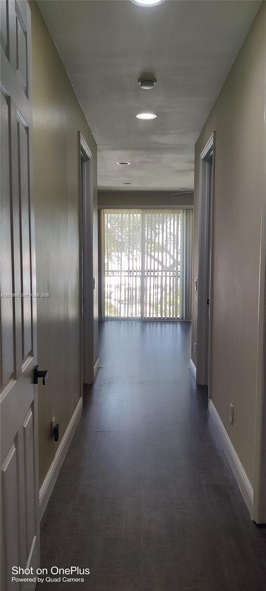 Hallway featuring recessed ceiling lighting, wood-finish flooring, and sliding glass doors with vertical blinds