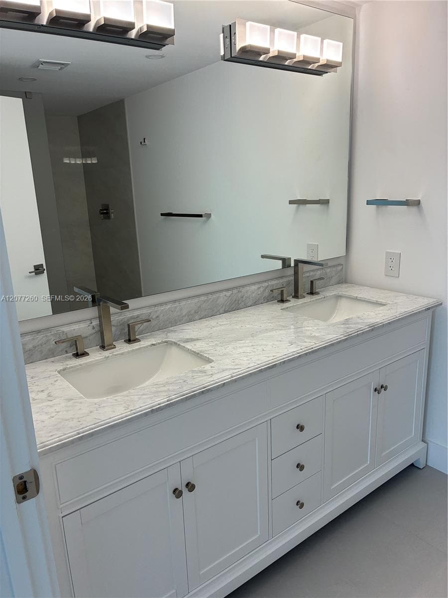Primary bathroom featuring double lavatories, comtempprary fixtures, marble countertops and ample storage.