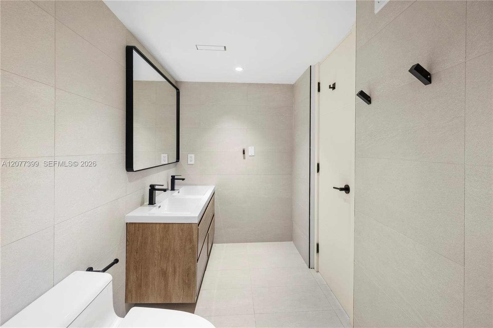 Double vanity with integrated sinks, wood-finish cabinetry, matte black hardware, and large-format wall tiling