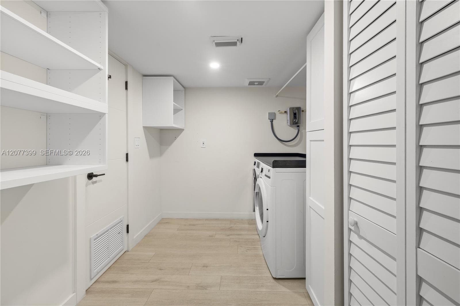 Laundry area featuring wood-finish flooring, built-in open shelving, louvered closet doors, and cabinetry