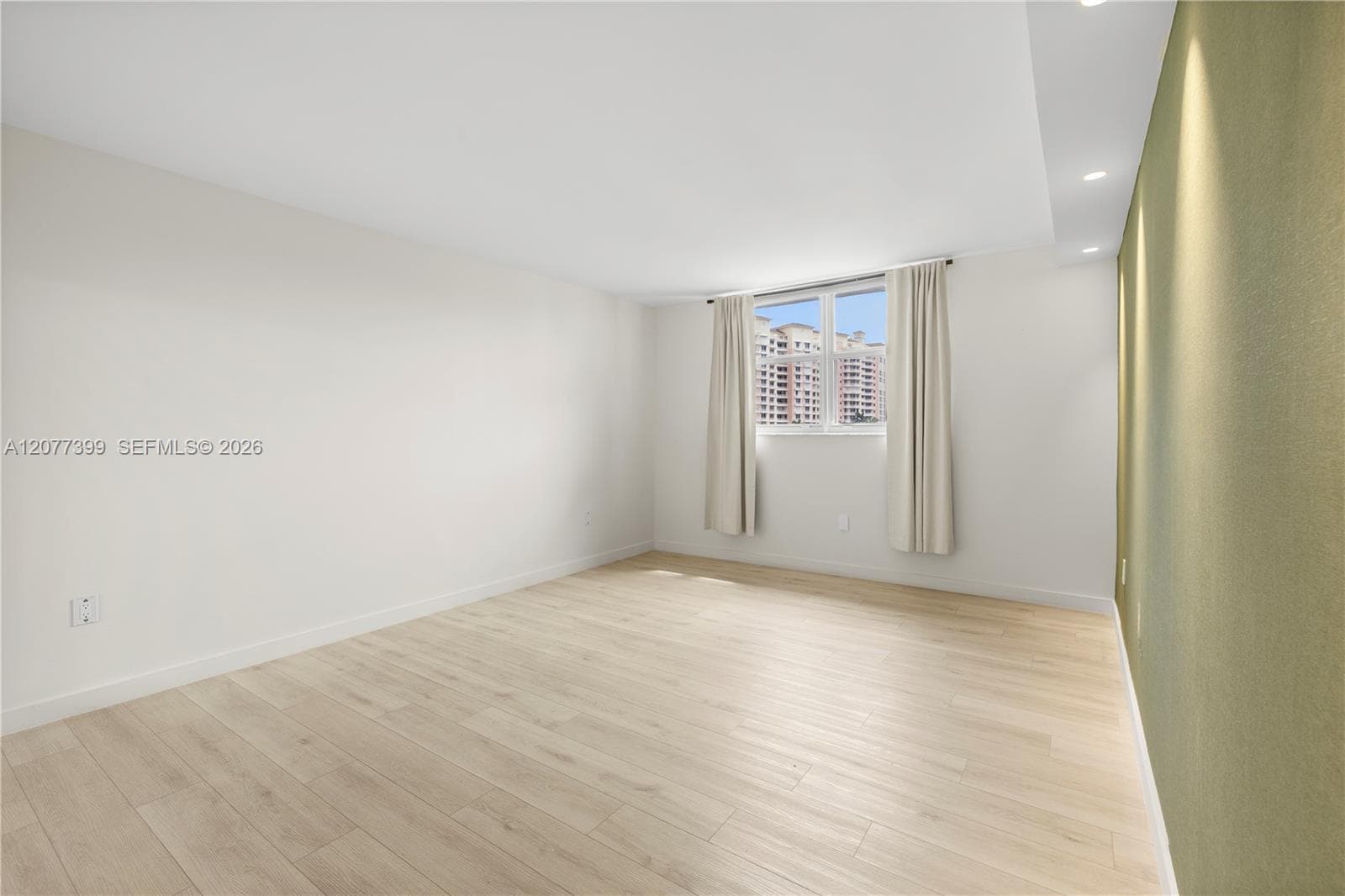 Interior space featuring light wood-finish flooring, a neutral color palette, recessed ceiling lighting, and a window with exterior building surroundings