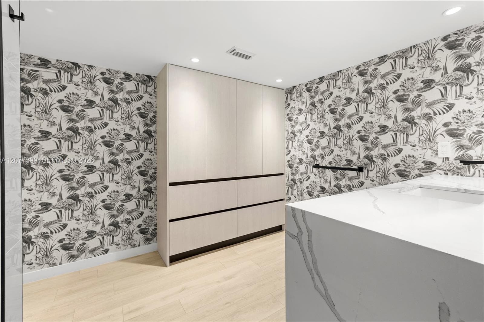 Built-in floor-to-ceiling cabinetry, patterned wall covering, wood-finish flooring, and a stone-topped vanity with an integrated basin