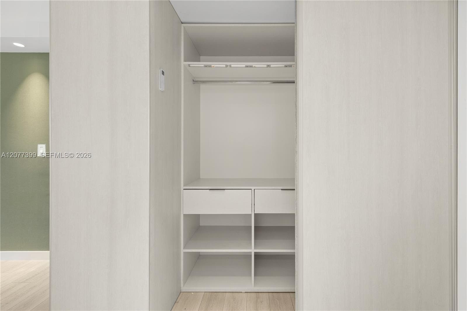 Custom built-in storage featuring light wood-finish cabinetry, two integrated drawers, open shelving, and a metal garment rod