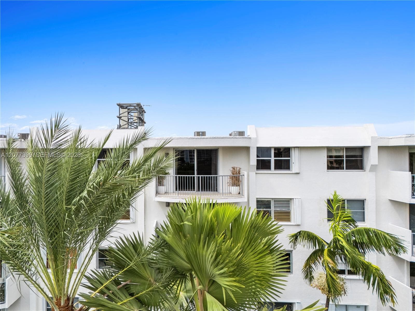 Stucco exterior building featuring private balconies with metal railings and palm tree landscaping