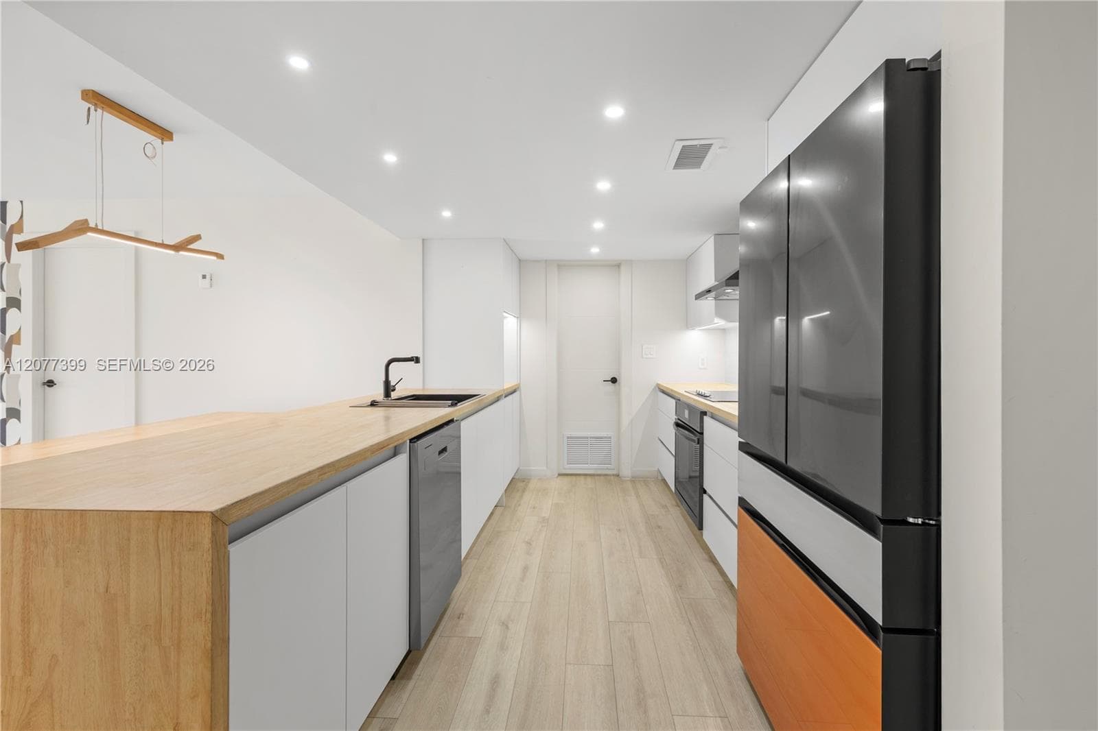 Modern kitchen featuring wood-finish countertops, matte black plumbing fixtures, integrated stainless steel appliances, flat-panel cabinetry, and wood-finish flooring