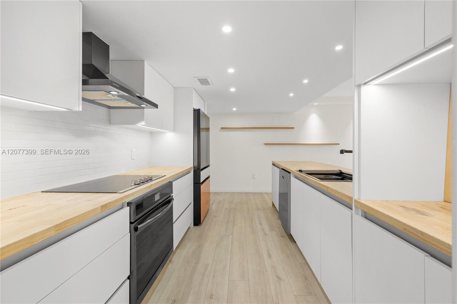 Kitchen featuring flat-panel white cabinetry, light-toned wood countertops, recessed lighting, integrated under-cabinet illumination, and wood-finish flooring