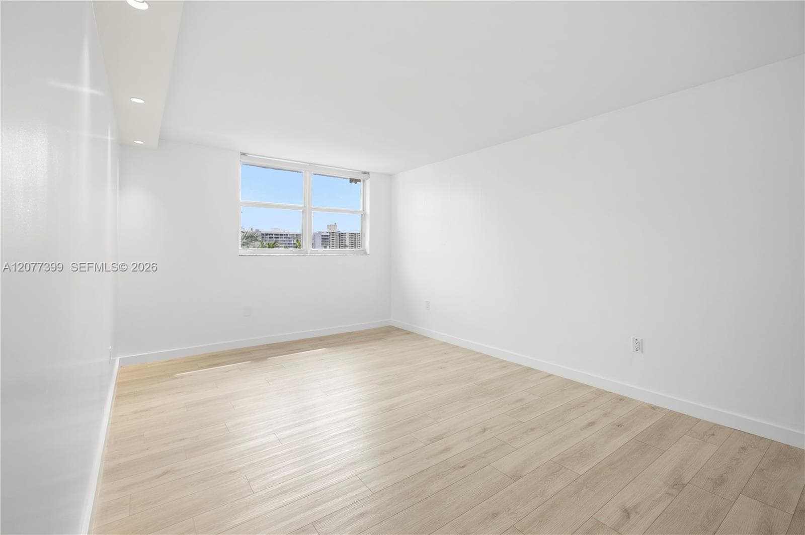 Neutral-toned interior space featuring wood-finish flooring, white walls, recessed ceiling lighting, and a multi-pane window