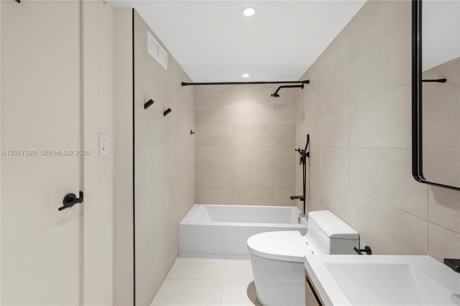 Bathroom featuring full-height light neutral wall tile, white soaking tub, matte black shower hardware, and a minimalist vanity