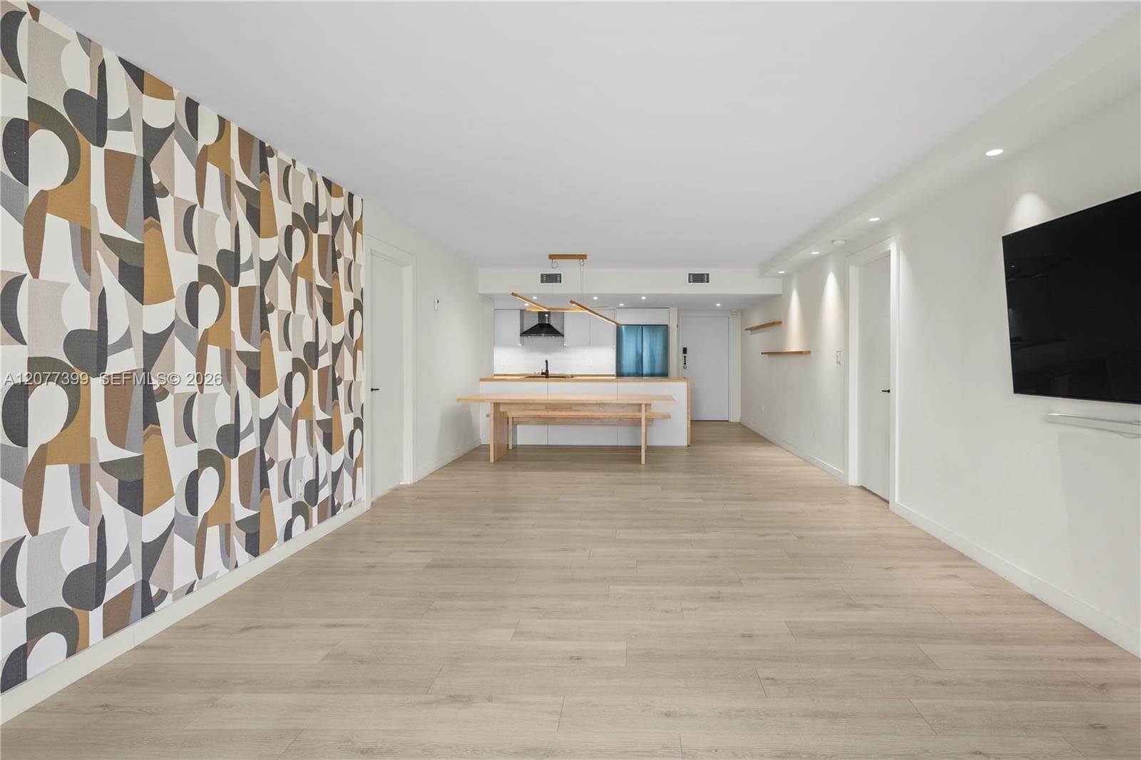 Open-concept interior featuring wood-finish flooring, a geometric patterned accent wall, recessed lighting, and wall-mounted shelving