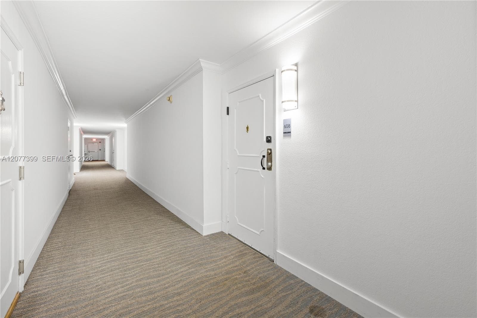 Hallway featuring white panel doors with decorative molding, wall-mounted sconce lighting, and neutral patterned carpeting