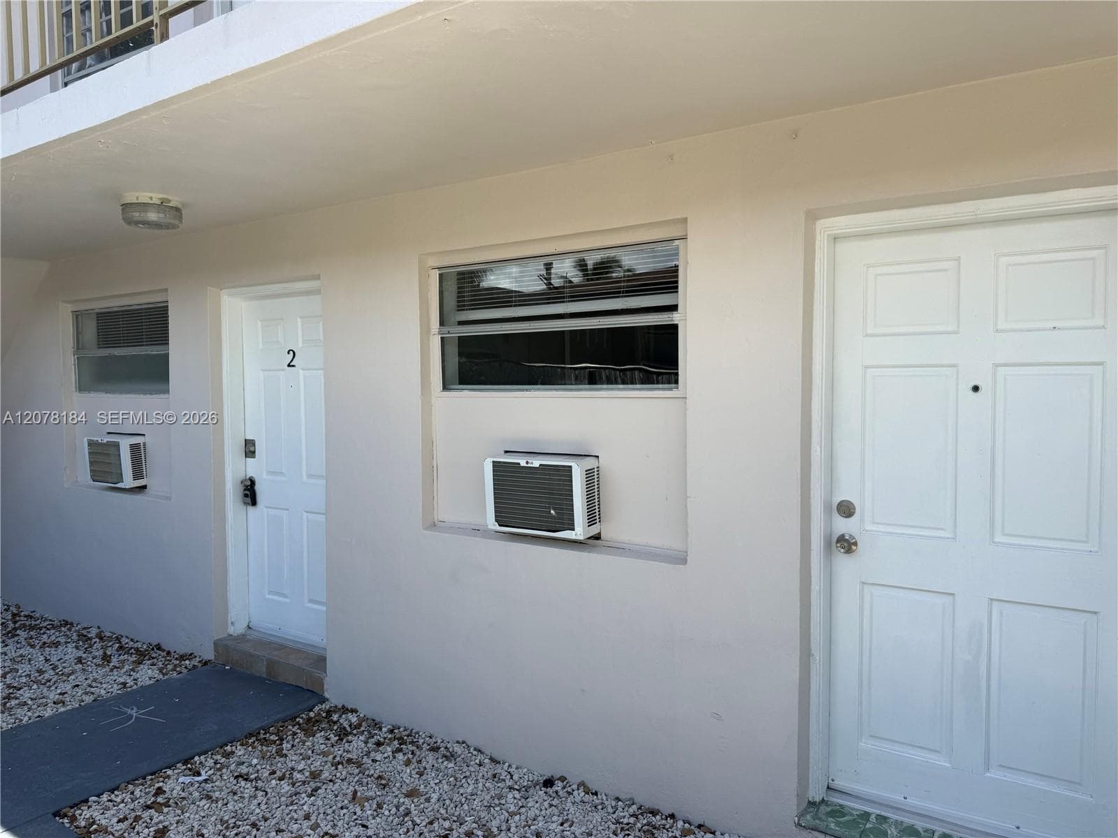 Exterior facade featuring dual paneled entry doors, horizontal slider windows, wall-mounted air conditioning units, and light-colored stucco finish