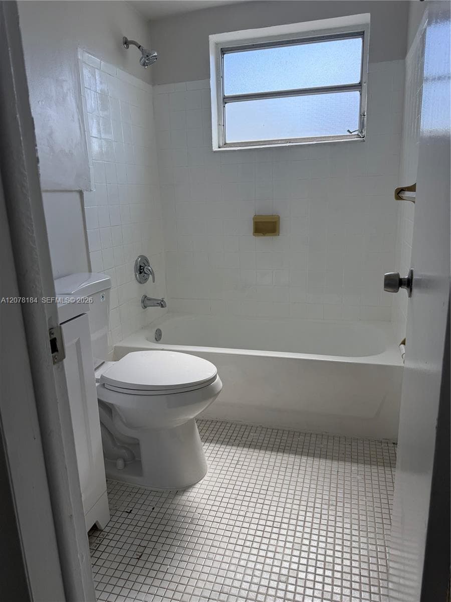 Bathroom featuring a white porcelain tub with integrated shower, square-grid tile flooring, white wall tiling, and an operable window