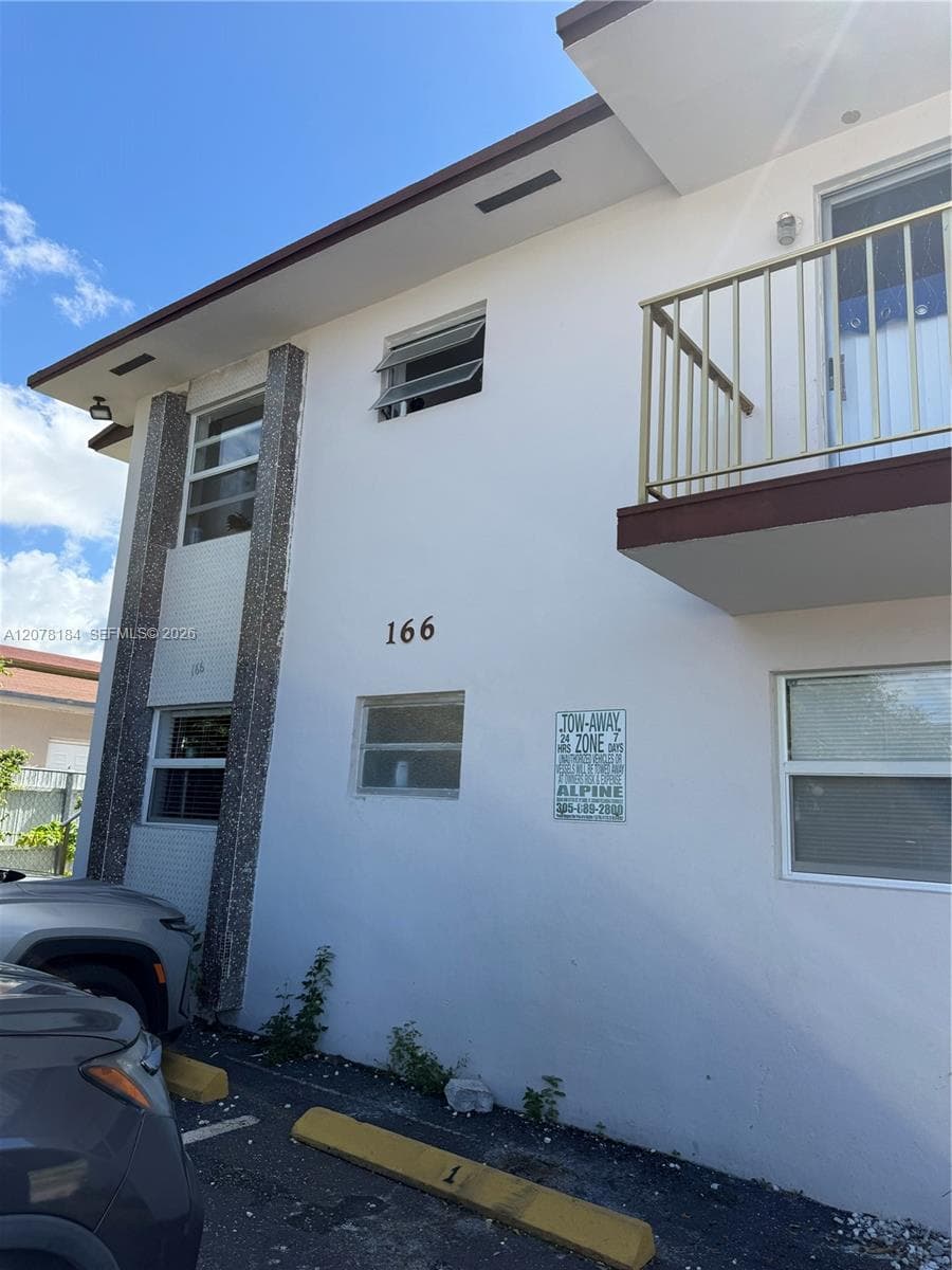 Two-story exterior featuring a smooth stucco finish, vertical stone-tiled accents, horizontal sliding windows, and an upper-level balcony with metal railing