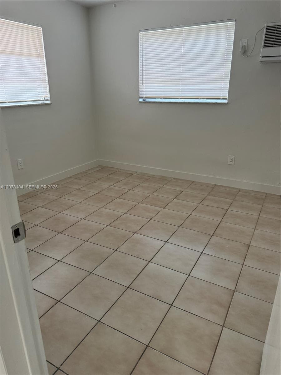 Neutral-toned ceramic tile flooring, two windows with horizontal blinds, and a wall-mounted air conditioning unit