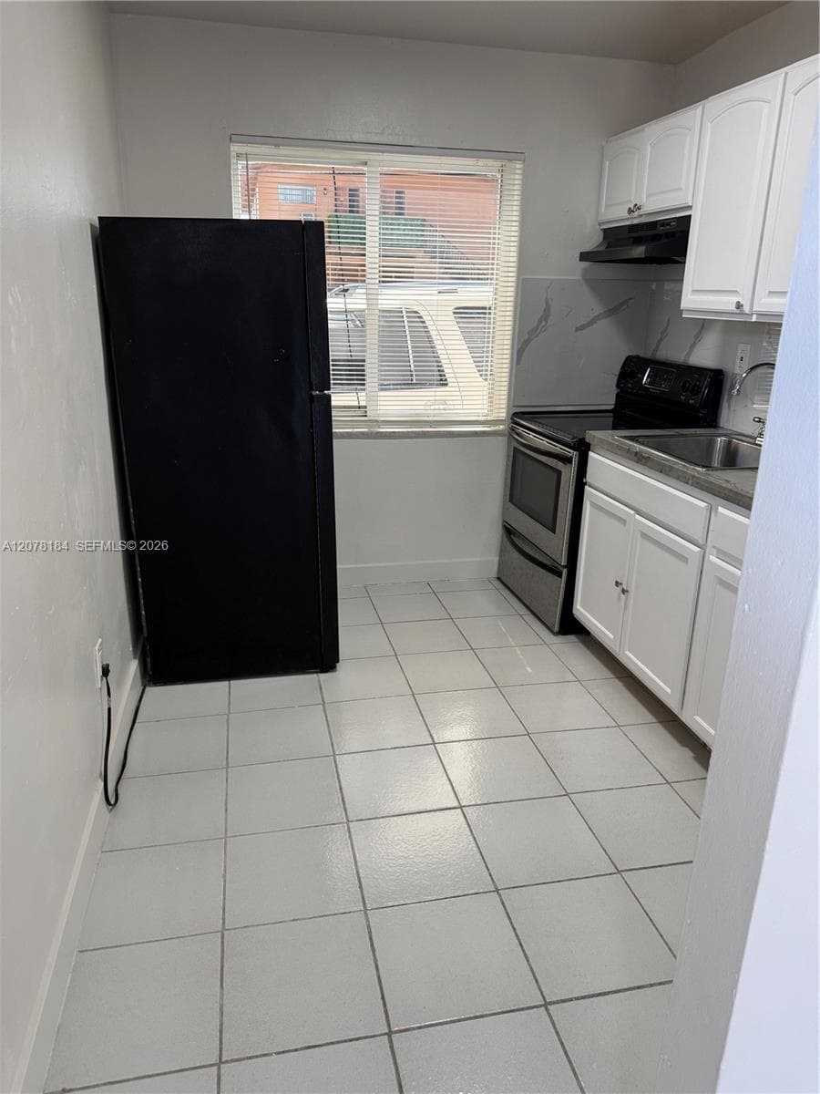 Kitchen featuring white cabinetry, solid surface countertops, a stainless steel oven, a black refrigerator, and tile flooring