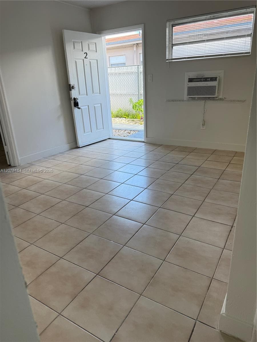 Interior space featuring neutral ceramic tile flooring, a six-panel entry door, and a horizontal window with integrated air conditioning unit