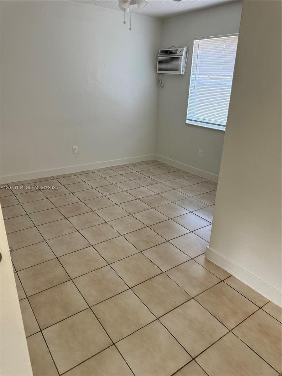 Neutral-toned tile flooring, white wall finish, window with horizontal blinds, and wall-mounted air conditioning unit
