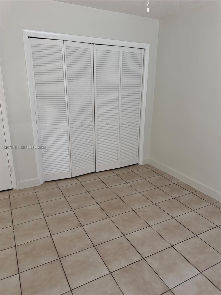 Four-panel louvered closet doors and neutral ceramic tile flooring