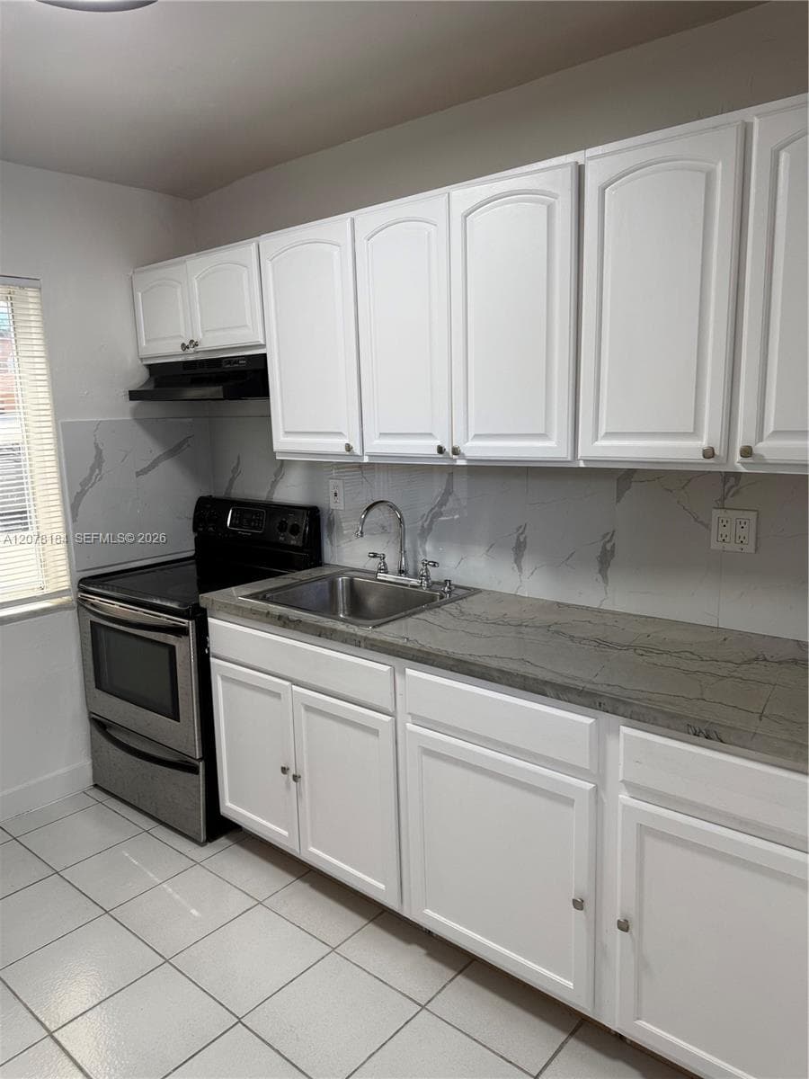 Kitchen featuring white shaker-style cabinetry, solid-surface countertops, stone-patterned backsplash, stainless steel range, and tile flooring