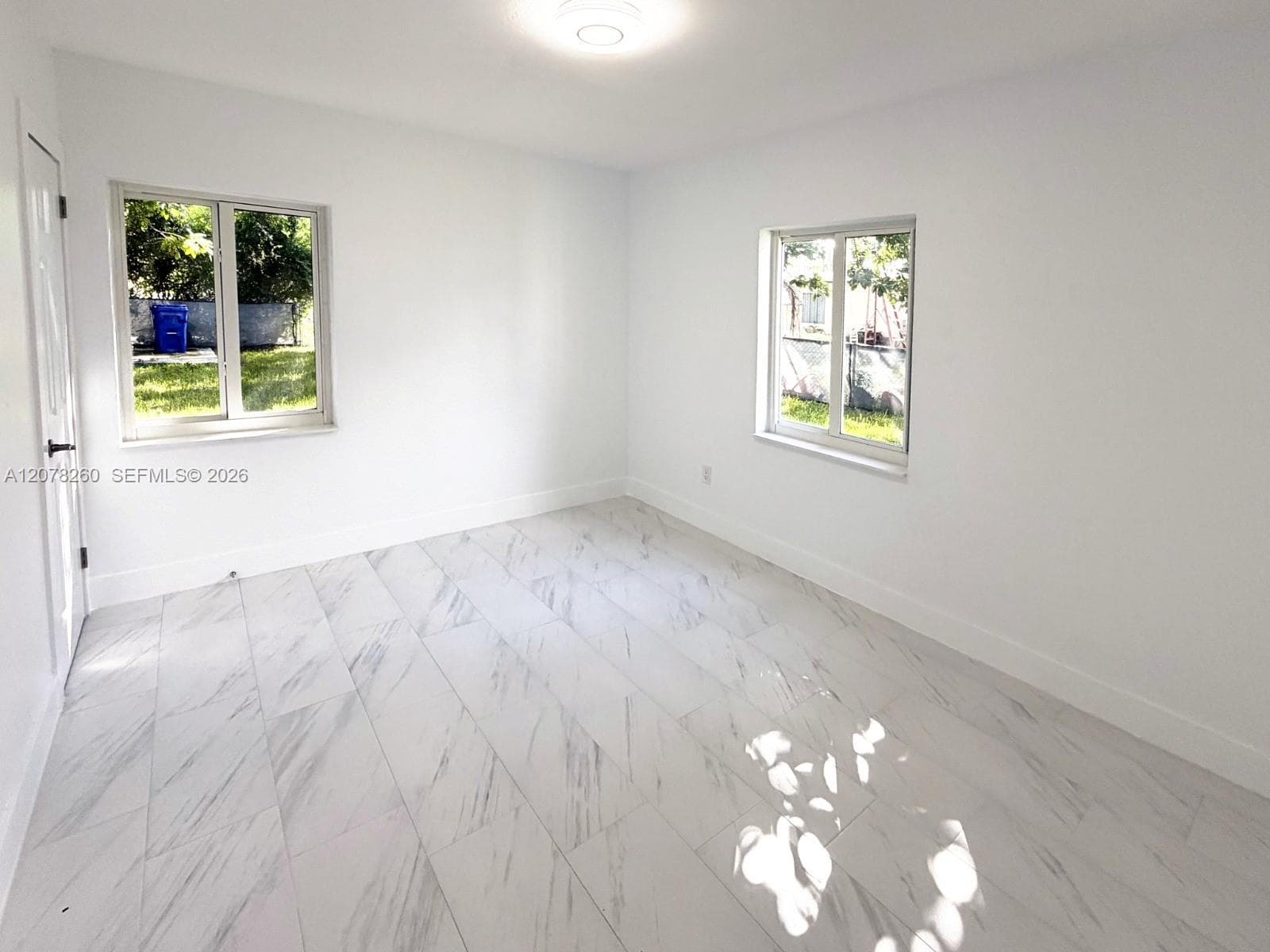 Neutral-toned room featuring large-format, light-veined tile flooring, dual windows, and a central flush-mount ceiling light fixture